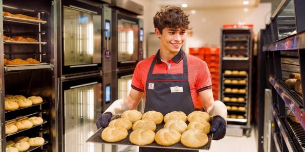 Junger Verkaufsmitarbeiter von Kaufland mit einem Blech frischgebackener Brötchen.
