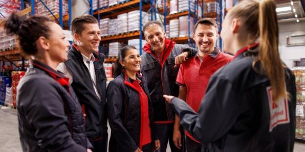 Sechs Logistikmitarbeiter von Kaufland im Gespräch. Im Hintergrund volle Lagerregale.