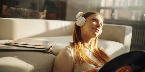 Frau sitzt vor einem Sofa und hört mit Kopfhörern Musik. In den Händen hält sie eine Schallplatte.