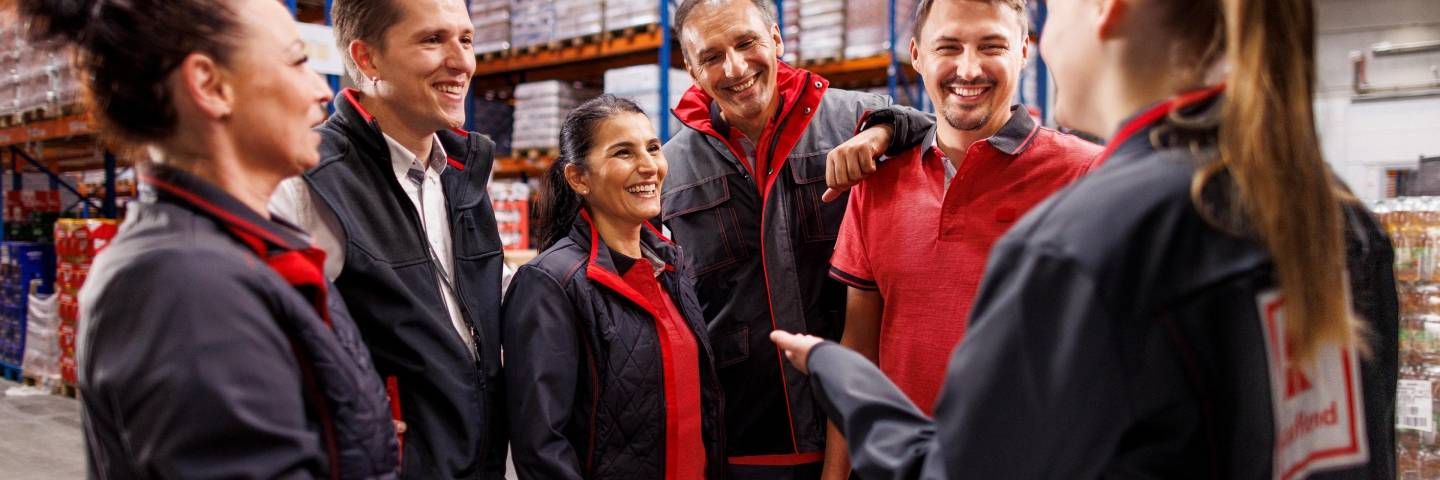 Sechs Logistikmitarbeiter von Kaufland im Gespräch. Im Hintergrund volle Lagerregale.