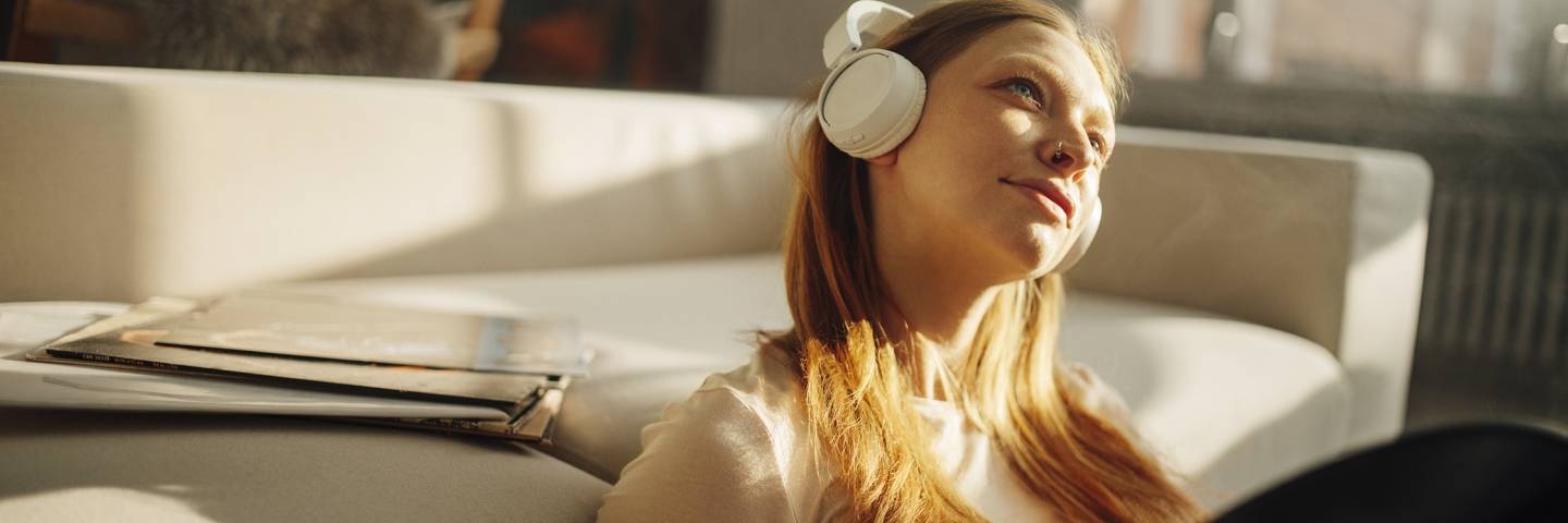Frau sitzt vor einem Sofa und hört mit Kopfhörern Musik. In den Händen hält sie eine Schallplatte.