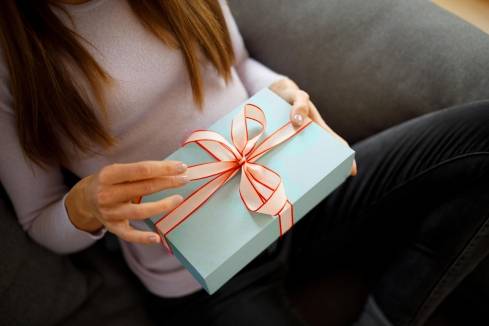 Frau sitzt auf einem Sofa und hält ein blau verpacktes Geschenk in der Hand.