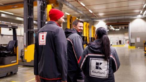 Drei Logistikmitarbeiter von Kaufland beim Gang durch eine Verladehalle.